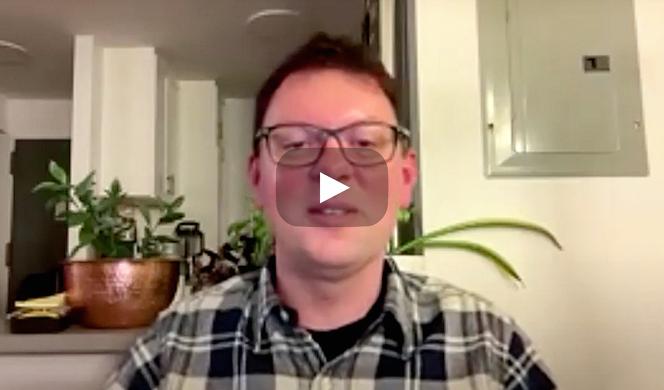A photo of Andrew Gordon Wilson with a play button superimposed on it